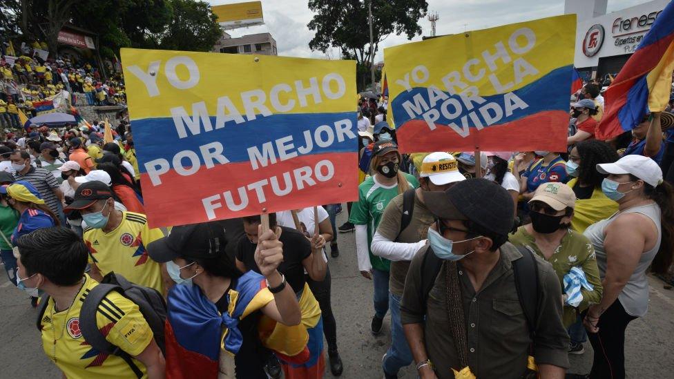 Demonstrators hold signs as they march through Cruz de la Loma towards Universidad del Valle during national strike against Ivan Duque's administration on May 12, 2021 in Cali, Colombia.