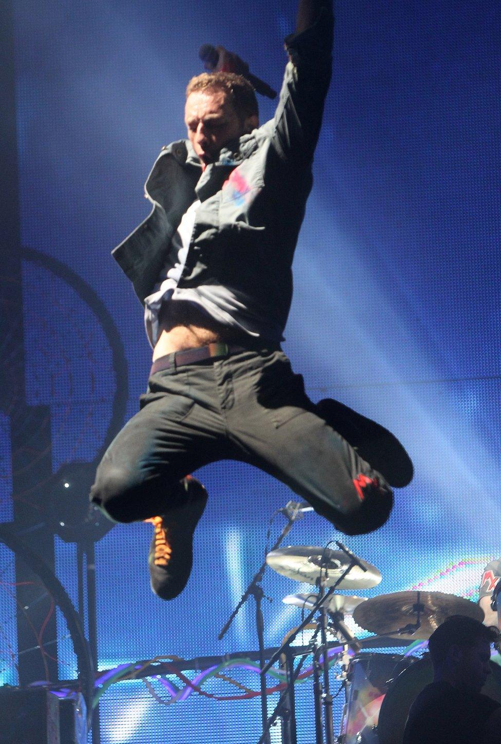 Chris Martin from Coldplay jumps into the air while on stage