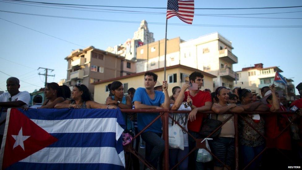 A man holds a US flag while gathering with others on a sidewalk near the US embassy (not pictured) in Havana, Cuba, on 14 August 2015.