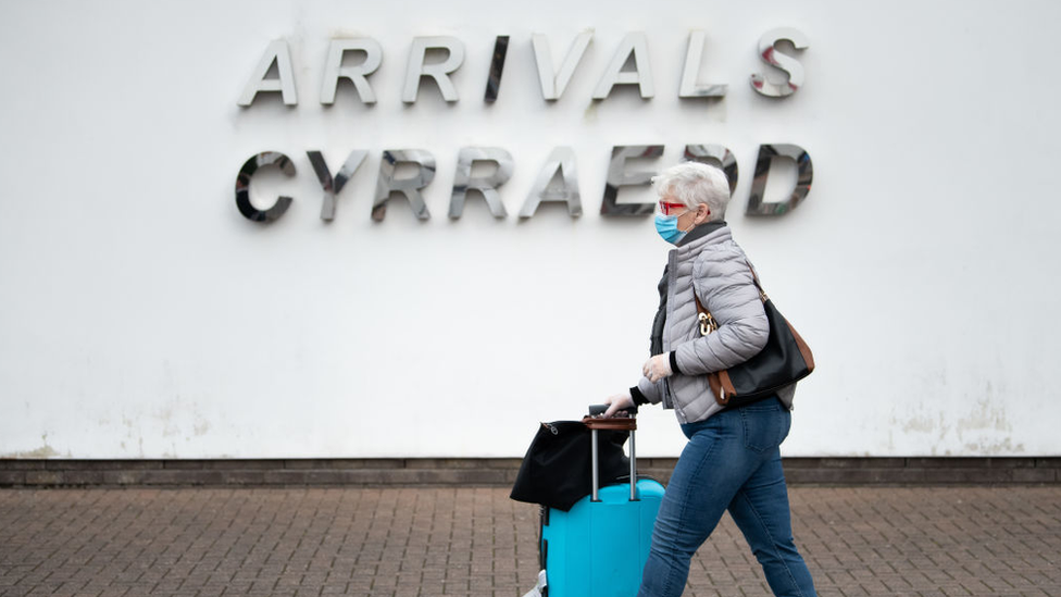 Woman in mask walking past arrivals sign at Cardiff Airport