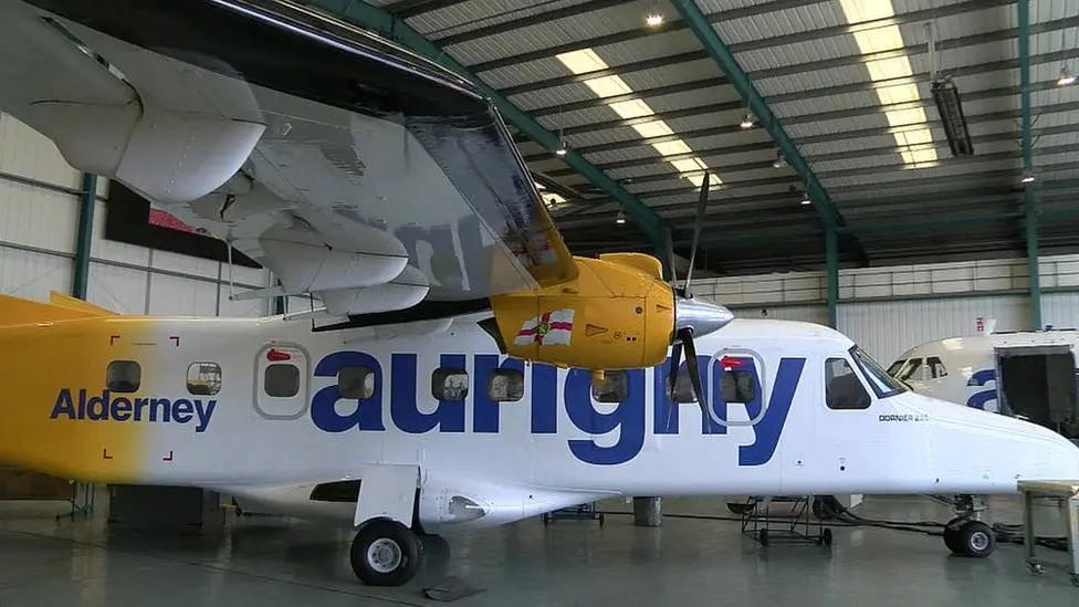 A white and yellow propeller plane with the words Aurigny sits in a hanger.