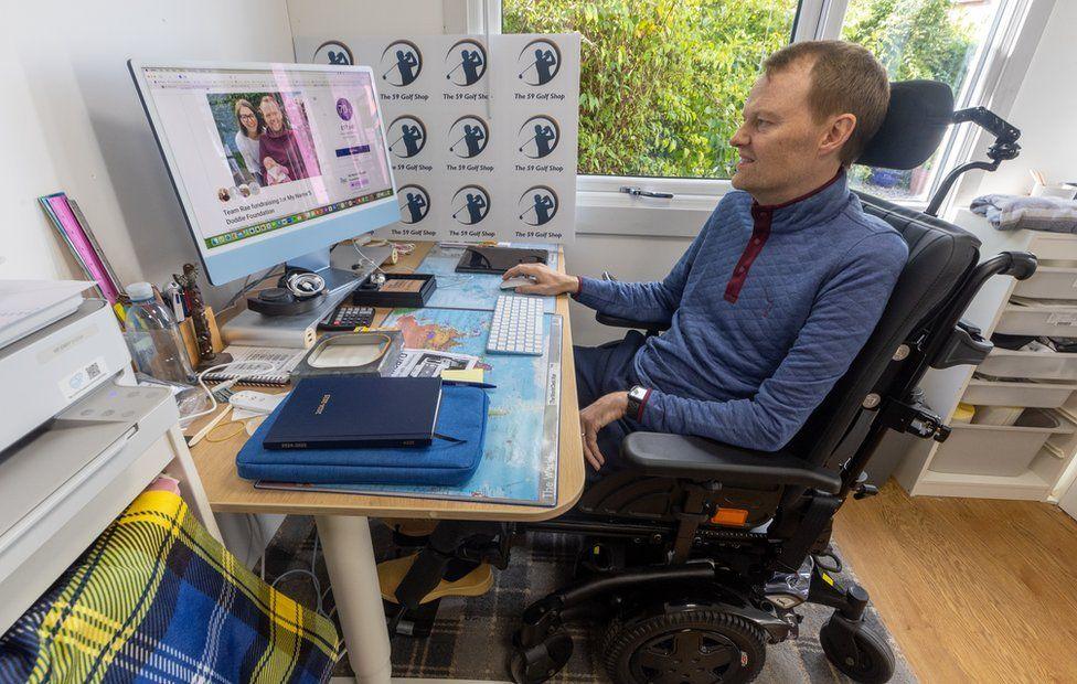 Scott Stewart sits in his wheelchair in his house in Stirling facing his computer where he works to earn a living for his family 