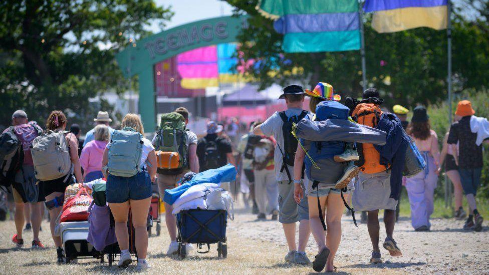 Festival-goers carrying tents across a field at the Isle of Wight festival