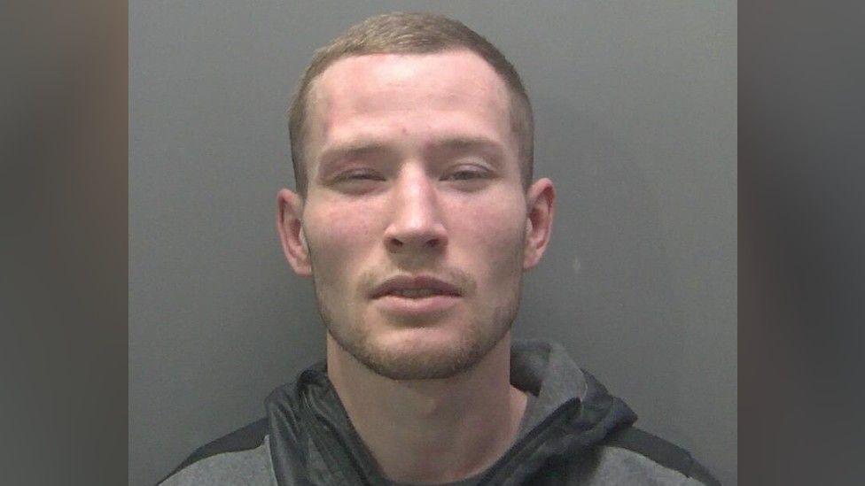Osvaldas Milius a man who is squinting at the camera. He is wearing a grey and black tracksuit jacket which has a hood.