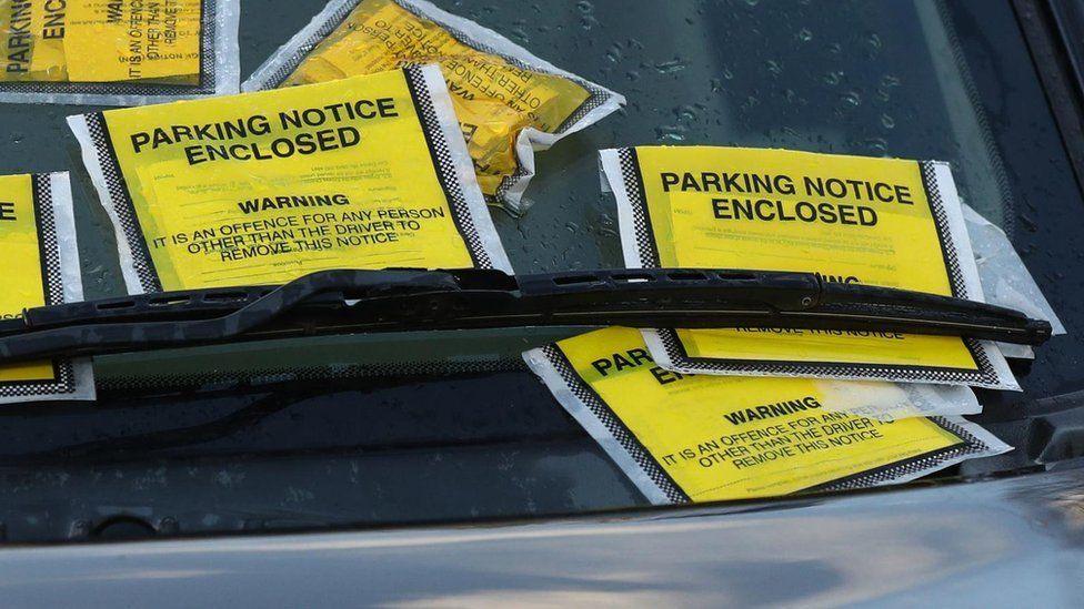 Several yellow parking notices are stuck on the windscreen of a car.