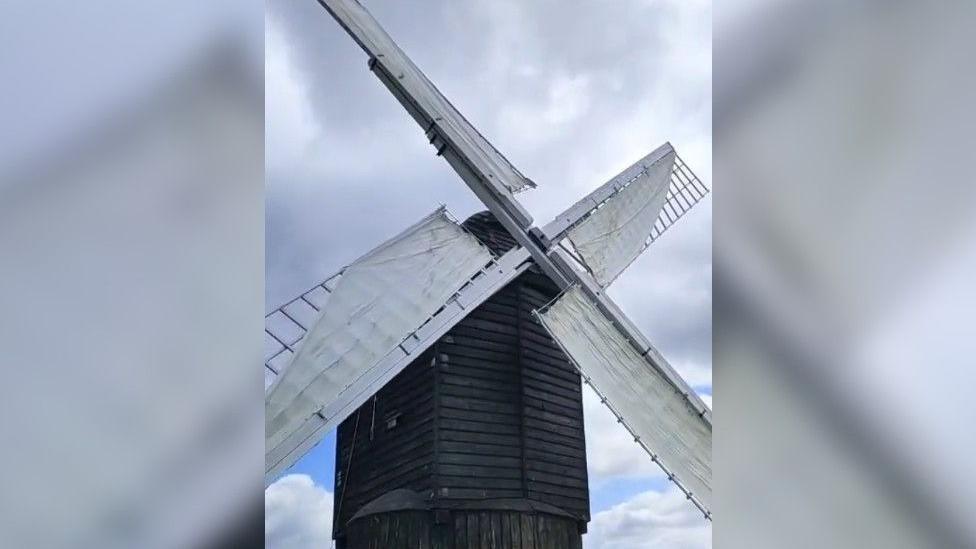 The windmill has a wooden frame which has been painted black. The rotating arms have been painted white and now have material wrapped around them to make them rotate in the wind.
