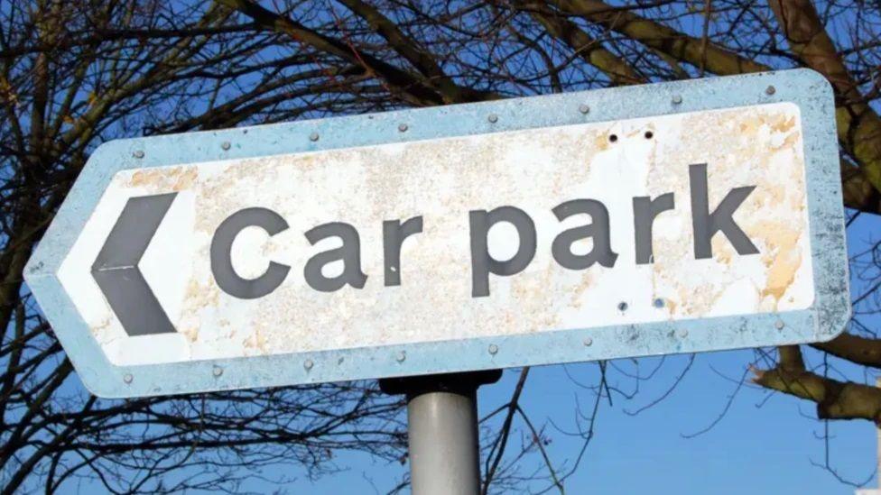 A photo of a car park sign with an arrow pointing left