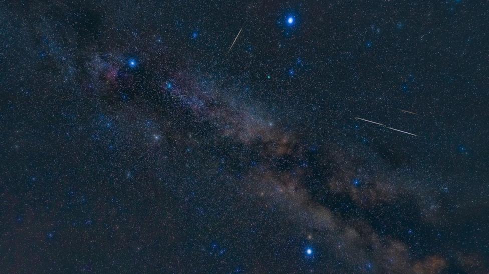 A picture of the night sky showing the three stars in the summer triangle. A meteor shower surrounds the stars.