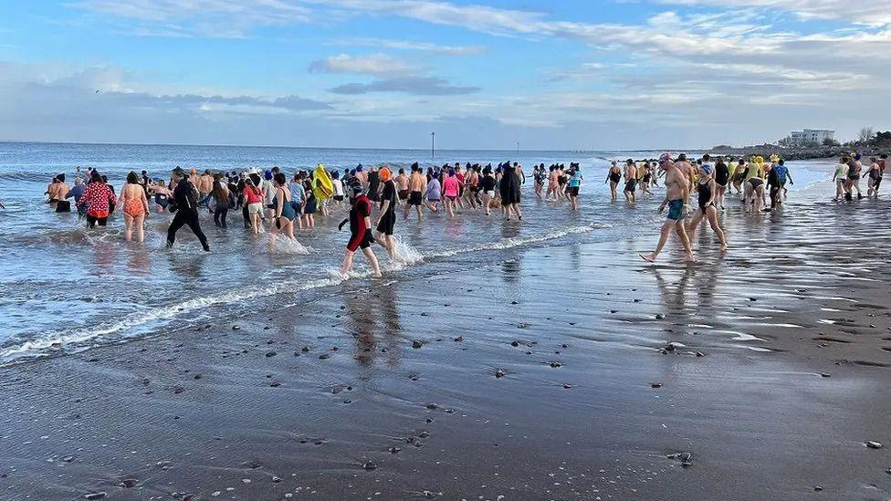 Hundreds of people on a beach walking towards the sea