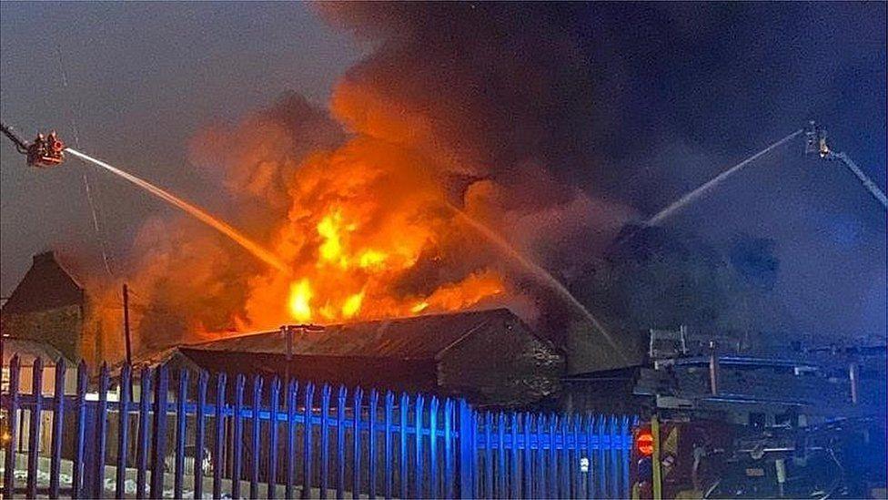 Firefighters spray water onto a burning factory from two aerial platforms either side of the building.