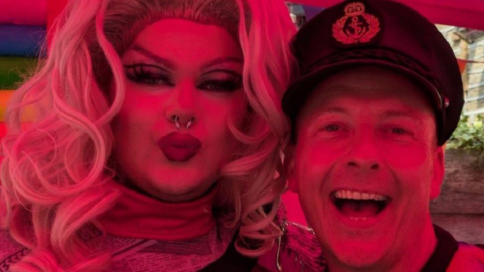 Maya Punion (L) and Captain Smash (R) posing for the camera and looking happy during the event. Maya has curly blonde hair and a nose ring, while Captain Smash has a captain's hat on.