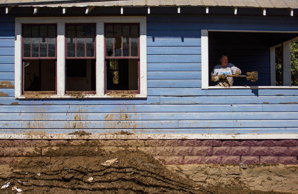 A woman uses a shovel to remove mud from a building on Main Street on October 3, 2024 in Marshall, North Carolina.  