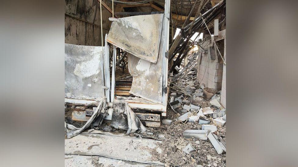 The inside of a large building that has been destroyed by a fire. Bricks and other debris are on the ground, and a burned-out structure to the left. 