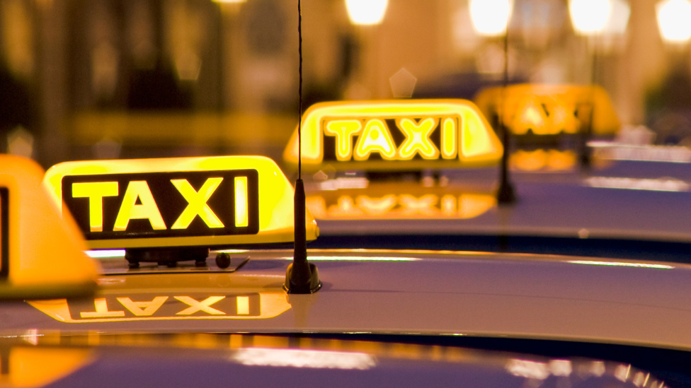 Taxis lined up in a row at night with neon yellow TAXI signs visible