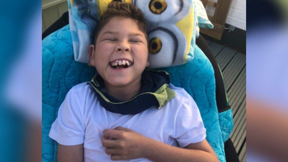 Brody smiling with his mouth open and eyes closed. He is wearing a white t shirt and has a minions blanket behind his head.