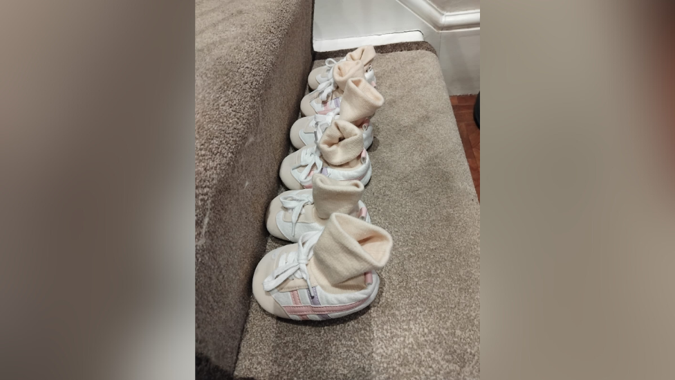 Three pairs of identical baby shoes and socks lined up along a carpeted stair
