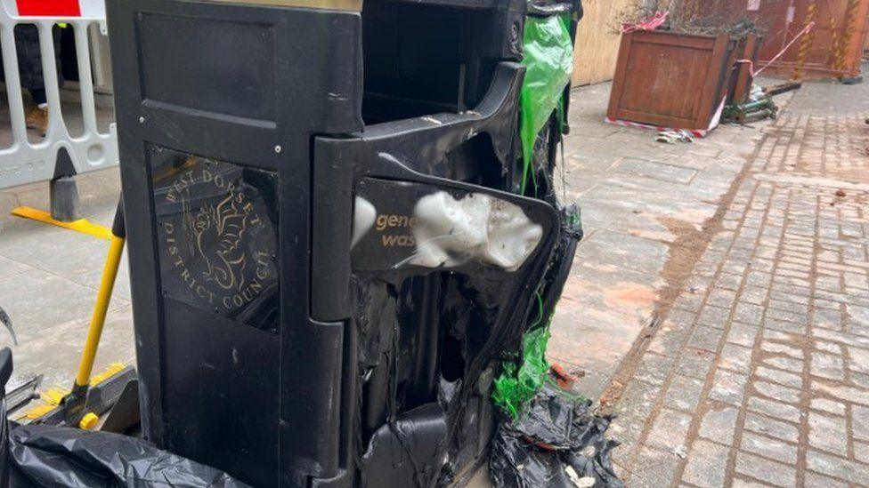 The front of a black council bin left melted and gaping open.