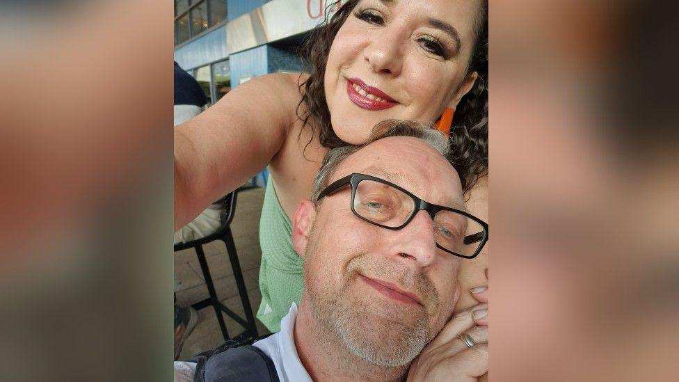 A selfie of Rohan Tarry and his wife. Rohan is leaning against his wife's arm and they are both smiling.