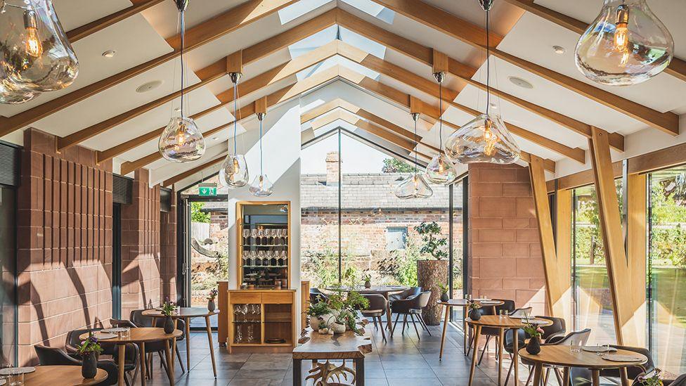 The restaurant at Moor Hall, a large wood and clay brick barn-style space with large glass windows, wooden tables and simple grey seating