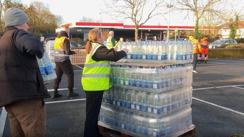 A pallet of water bottles being handed out to people in a car park