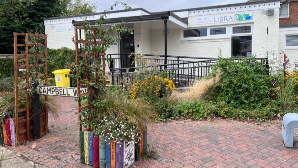 Ornamental books either side of the paved entrance with planting up to a single storey cream building