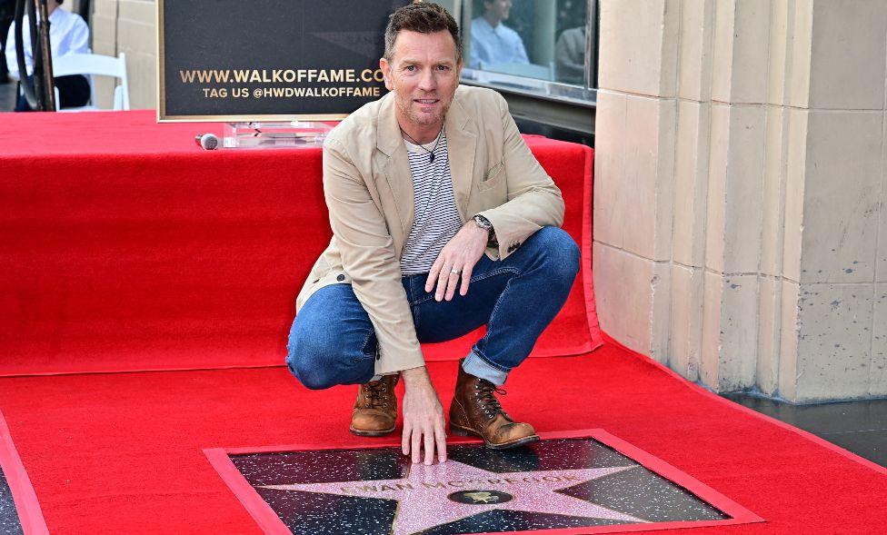 British actor Ewan McGregor touches his star during his Hollywood Walk of Fame Star ceremony in Hollywood, California. He is wearing brown boots, jeans and a beige jacket.