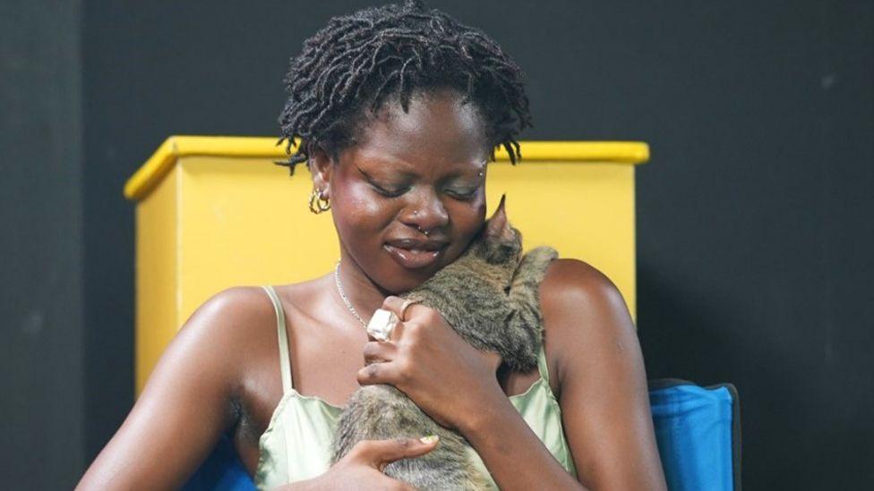 Mistura Ibrahim sits on a chair hugging a tabby cat