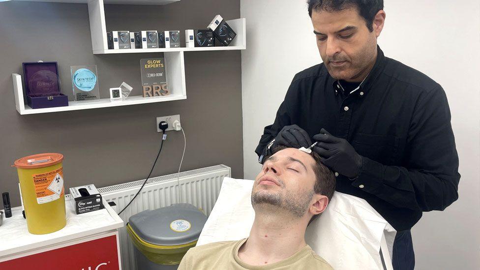 Dr Javen Hussain is injecting his patient, Ven, in his forehead with a botox needle.