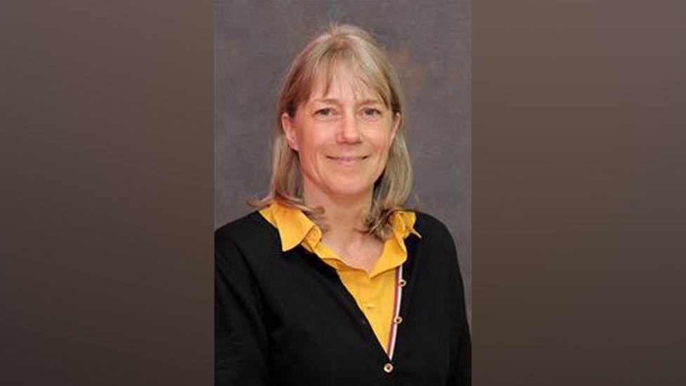 A picture of Councillor Sally Symington, she has blonde hair with a fringe, and her hair is down to her neck. She is wearing a black cardigan with a yellow shirt underneath.