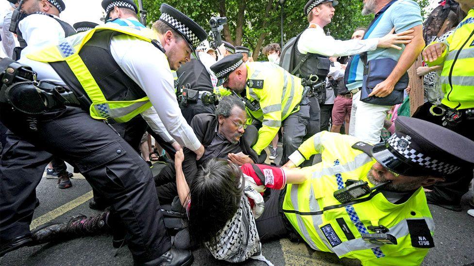 Police officers - one of whom is on the ground - hold down protesters
