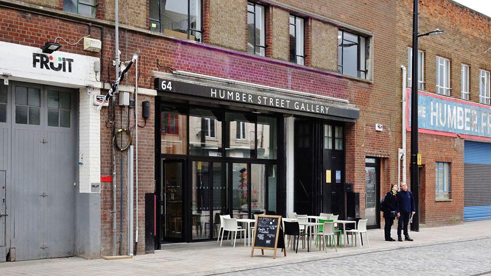 Exterior view of the glass-fronted Humber Street Gallery with tables and chairs outside on the pavement