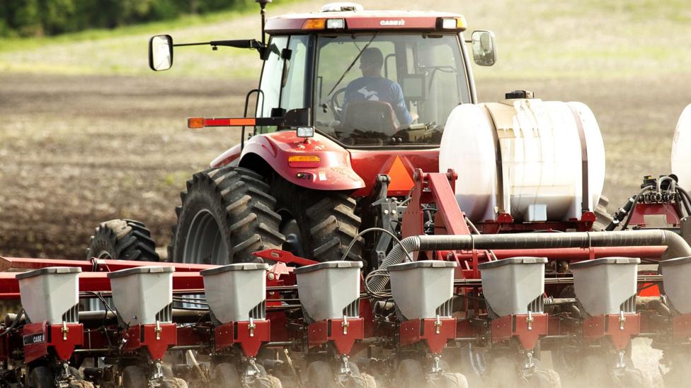 A farmer sits in a tractor in Michigan whilst spraying fertiliser on his crops