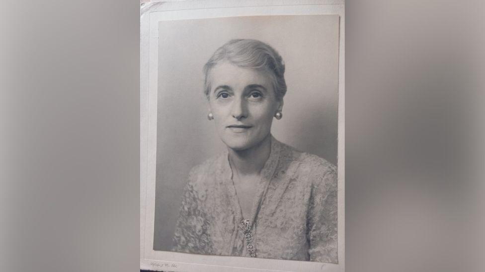 Lydia, to whom Stanley apologised in his postcard. It is a black and white photograph of an adult woman with her hair tied back. She is wearing a lace blouse and has chunky earrings on. 