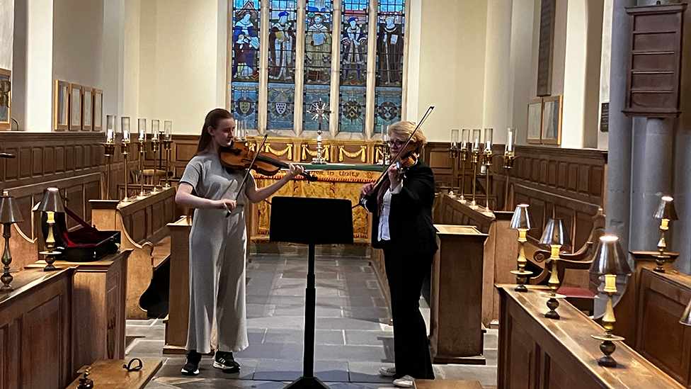 Elisabeth and Marion playing together in a church, with a stained glass window behind them