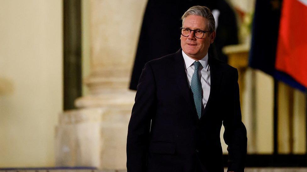 Britain's Prime Minister Keir Starmer wearing a suit and tie as he looks out to media while walking out of the Elysee Palace in Paris