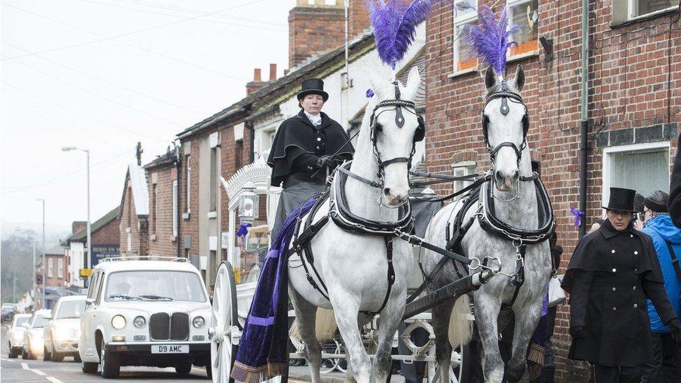 The funeral for teenager Kayleigh Haywood. Her coffin was pulled in a white carriage by two white horses. A white car can be seen on the road behind the carriage as part of the procession.