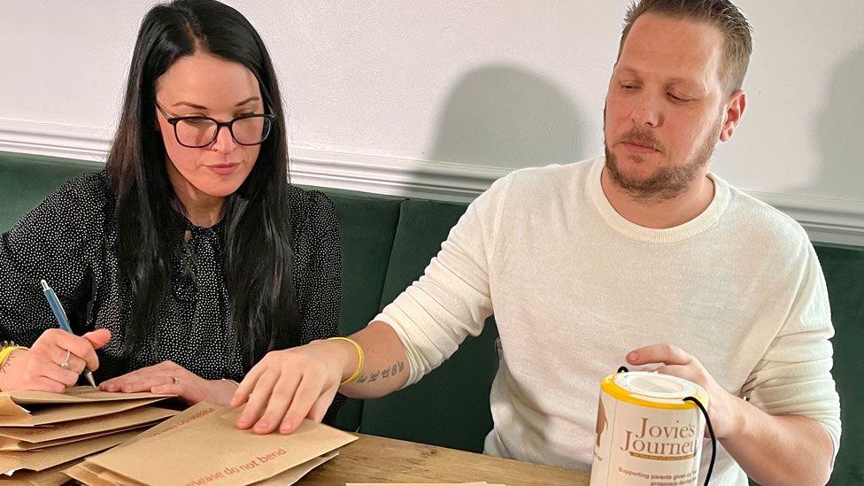 Deborah and Chris Manning addressing envelopes at a pine table