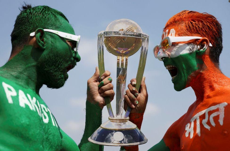 Cricket fans, Arun Haryani (Right) and Anil Advani (Left) pose for a photograph with a replica trophy after painting their bodies in the Indian and Pakistani national flag colours, ahead of the match between India and Pakistan in the ICC World Cup, in Ahmedabad, India, October 11, 2023. 