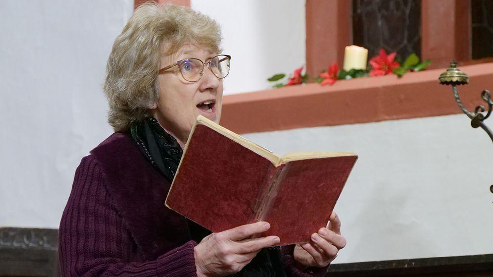 dynes yn canu mewn capel