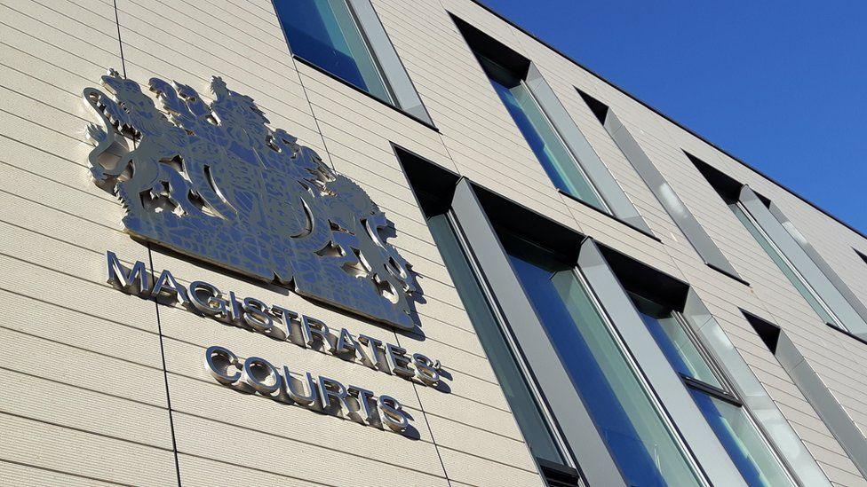 The side of Chelmsford Magistrates' Court, which is white with large windows. It has a large crest on the wall with the lettering "magistrates' courts".