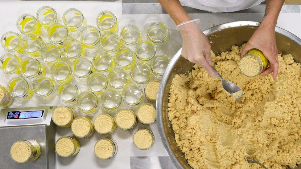 A body scrub mix is scooped into jars