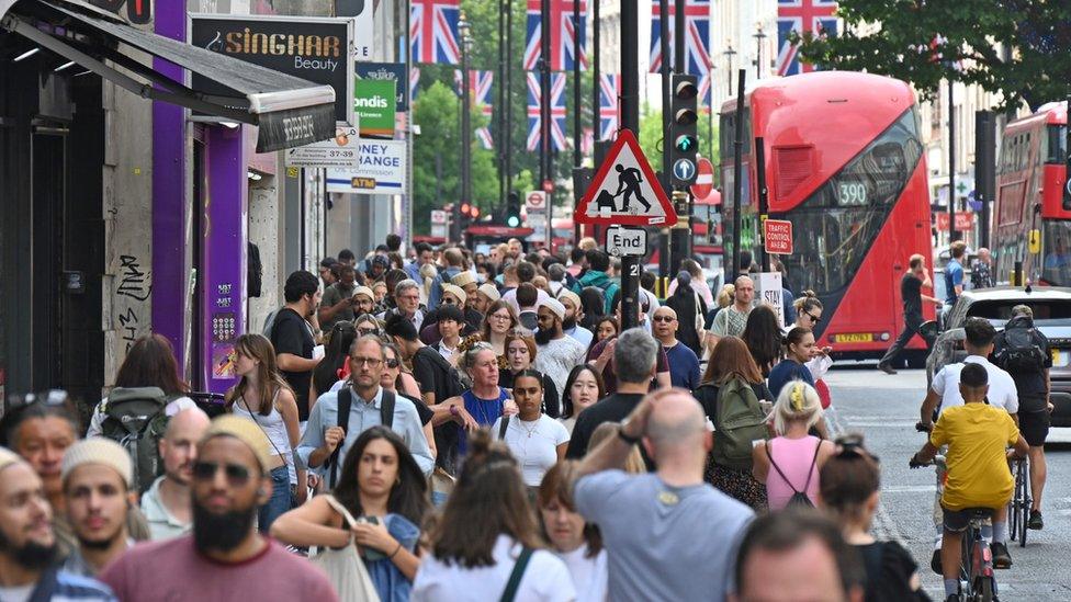 Crowds of shoppers on Oxford Street in London, with a red double decker bus visible in the background.