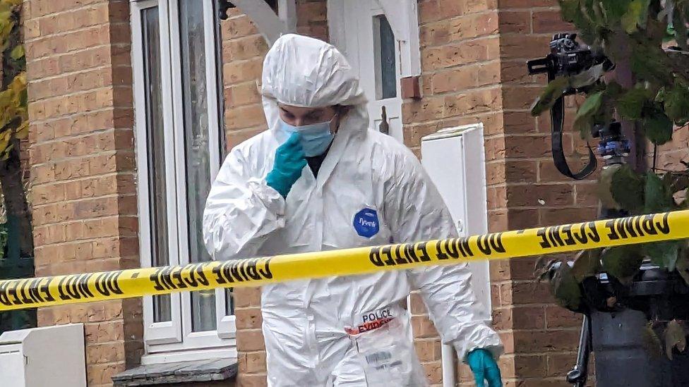 A forensic investigator in a white suit leaving a house