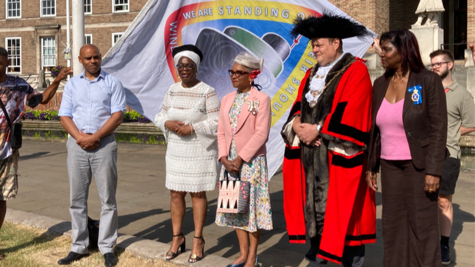 Five people standing by the Windrush flag