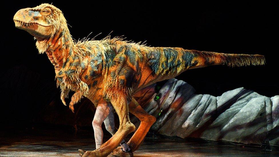 A life-size baby T Rex dinosaur puppet on stage