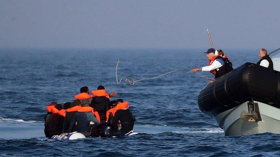 Migrants on a dinghy being helped by UK Border Force officers