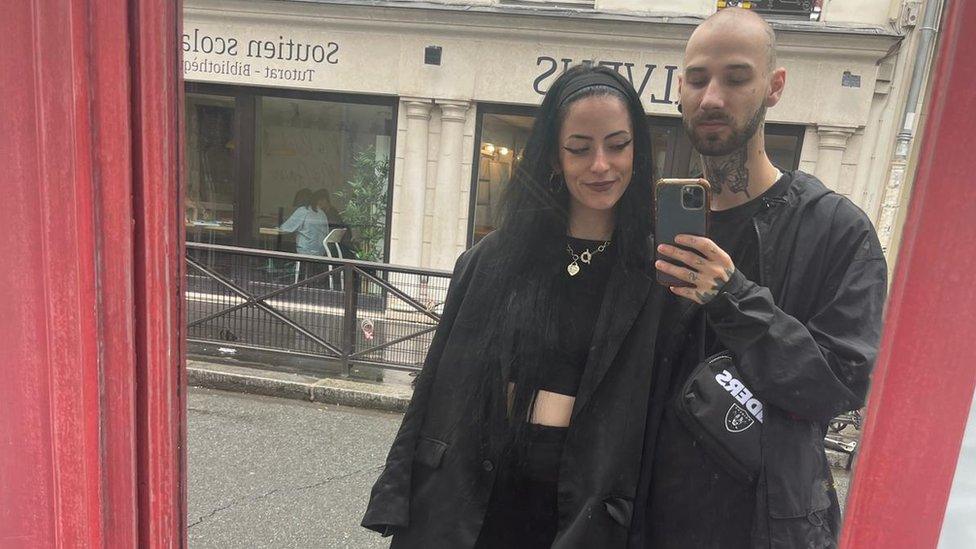 James Cox and his girlfriend take a picture in a mirror, wearing all black clothing