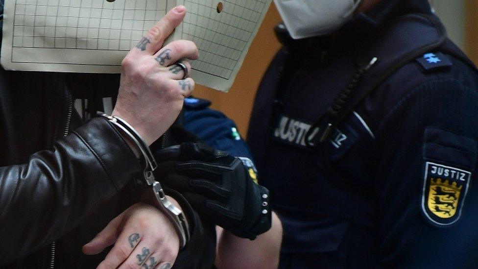 A defendant covers his face with a file as he is led into the courtroom