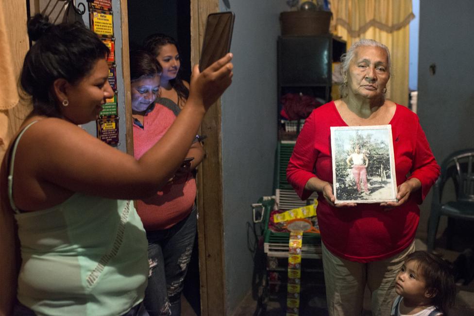 Edita Maldonado holds a picture of her late daughter Rosa while Sirly holds up her phone to provide light and Sandra and Greicy watch