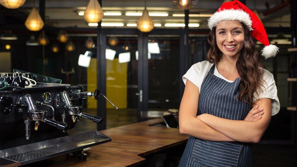 A woman working in a coffee shop wearing a Santa hat